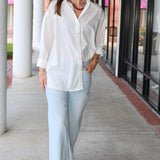 Bea Shirt, NIA - white button down shirt and light blue PISTOLA jeans standing on a sidewalk.