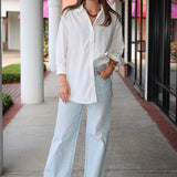 Bea Shirt, NIA - white button down shirt and light blue jeans standing on a sidewalk.