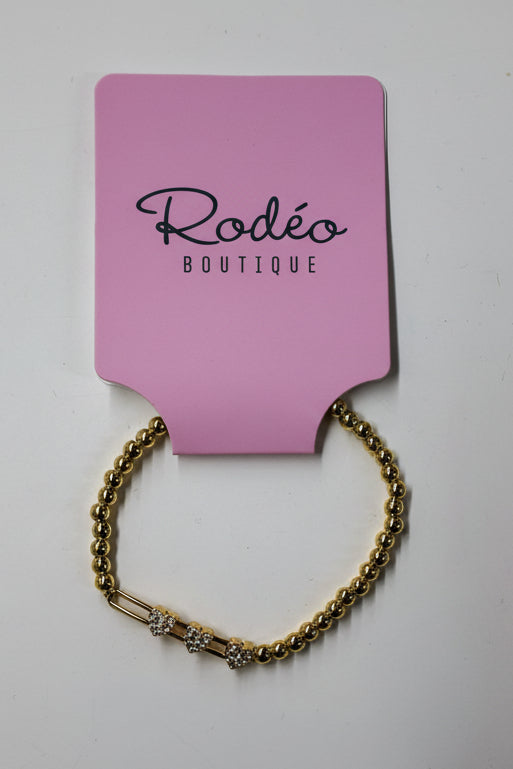 Gold bracelet on a pink card with 'Rodeo Boutique' branding on a white background