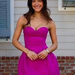 Woman wearing a bright pink strapless mini dress standing in front of a house.
