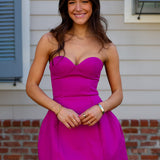 Woman wearing a bright pink strapless mini dress standing in front of a house.