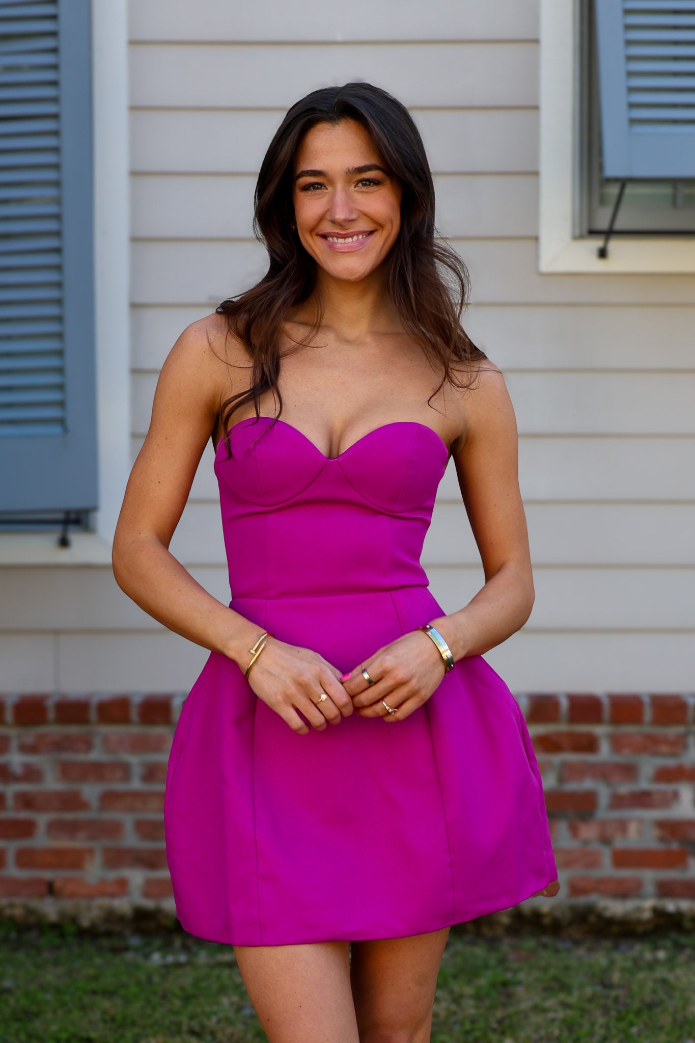 Woman wearing a bright pink strapless mini dress standing in front of a house.