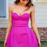 Woman wearing a bright pink strapless dress standing outdoors.