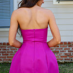 Woman wearing a bright pink strapless dress standing outdoors.
