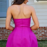 Woman wearing a bright pink strapless dress standing outdoors.