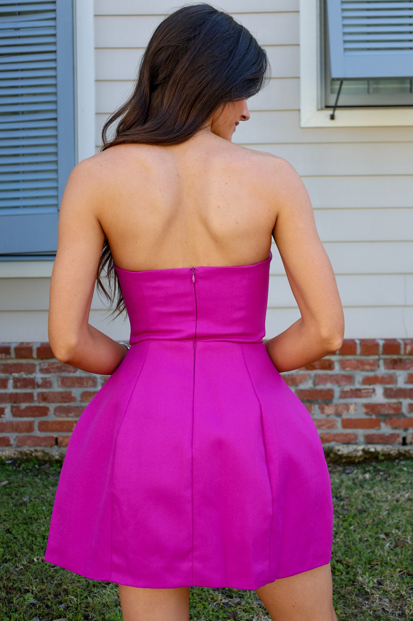 Woman wearing a bright pink strapless dress standing outdoors.