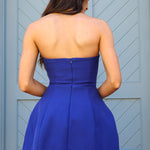 Woman wearing a blue strapless dress standing in front of a gray door.