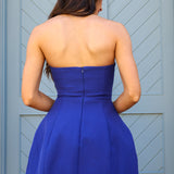 Woman wearing a blue strapless dress standing in front of a gray door.