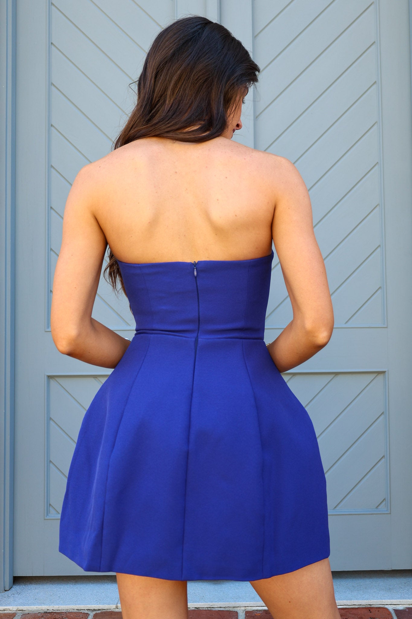 Woman wearing a blue strapless dress standing in front of a gray door.