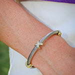 A close-up of a person's wrist wearing a silver cable-style bracelet with gold-toned ends and a small star charm set with clear stones.