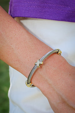 A close-up of a person's wrist wearing a silver cable-style bracelet with gold-toned ends and a small star charm set with clear stones.