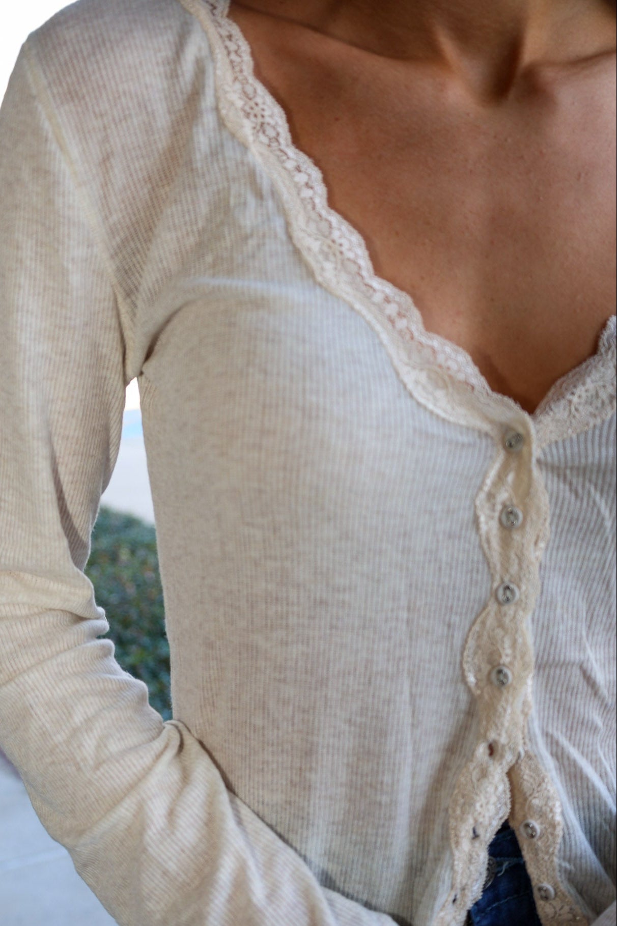 Close-up of a person wearing a beige long-sleeve top with lace trim.