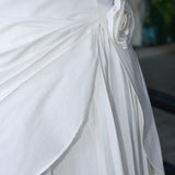Close-up of a white draped skirt with pleated detailing and a side fabric flower embellishment, shown on a model.
