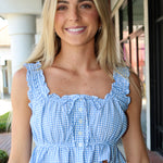 Woman wearing a blue checkered top with ruffled details outdoors.