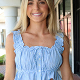 Woman wearing a blue checkered top with ruffled details outdoors.