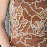 Close-up of a strapless dress featuring a brown suede-like base with an intricate cream crochet lace overlay pattern.