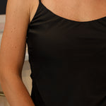 A woman wearing a black-colored satin camisole top and light-wash denim jeans at Rodeo Boutique.
