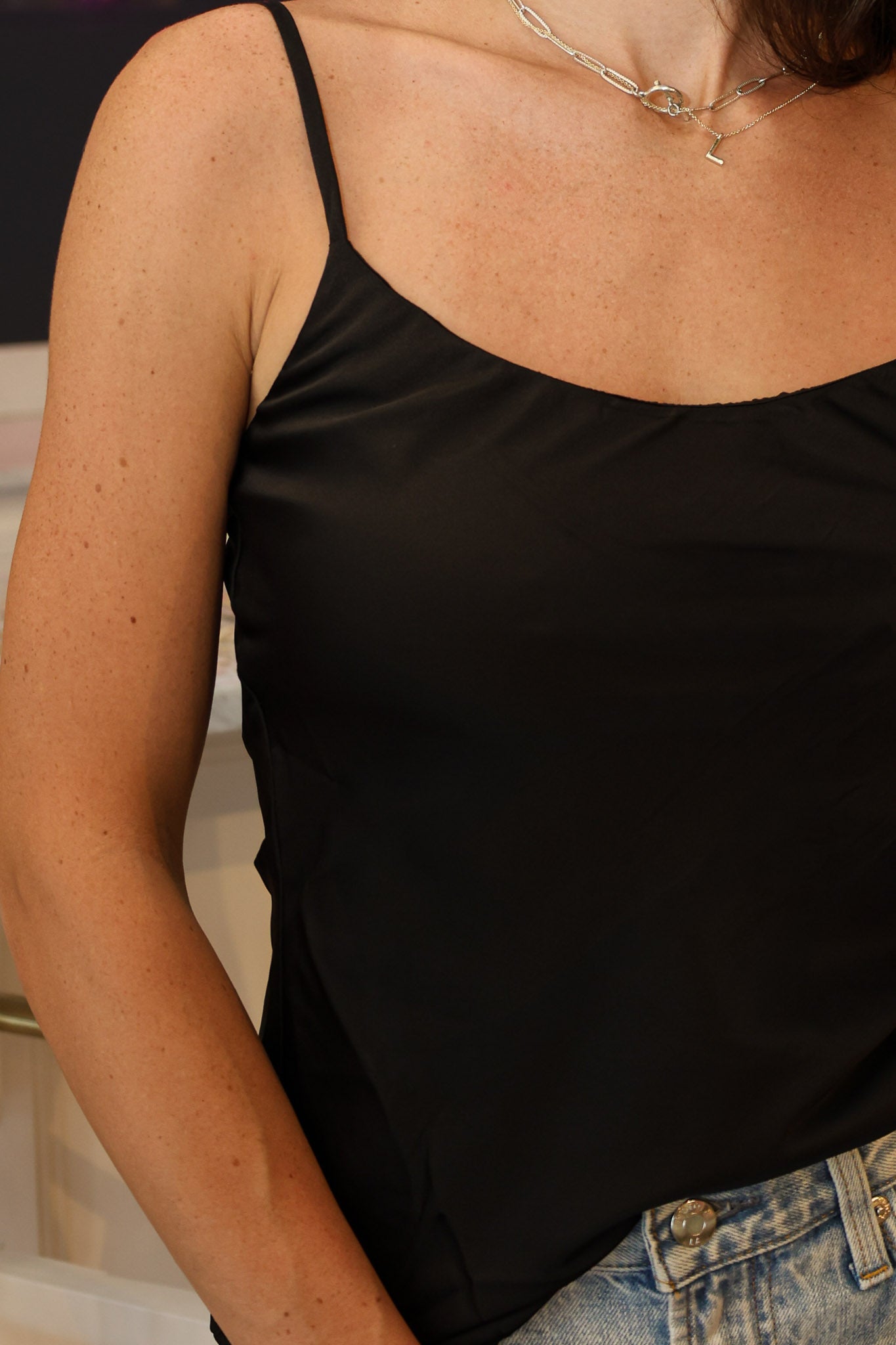A woman wearing a black-colored satin camisole top and light-wash denim jeans at Rodeo Boutique.