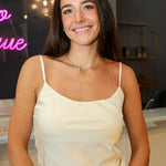A woman wearing a cream-colored satin camisole top and light-wash denim jeans at Rodeo Boutique.