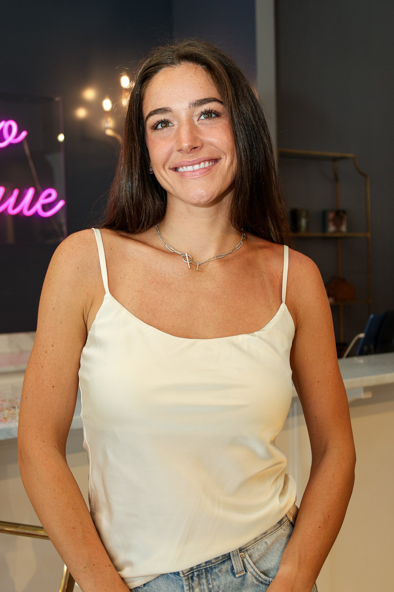 A woman wearing a cream-colored satin camisole top and light-wash denim jeans at Rodeo Boutique.