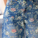 Close-up of a person wearing blue floral jeans with a pink and green rose print, paired with a light beige top.
