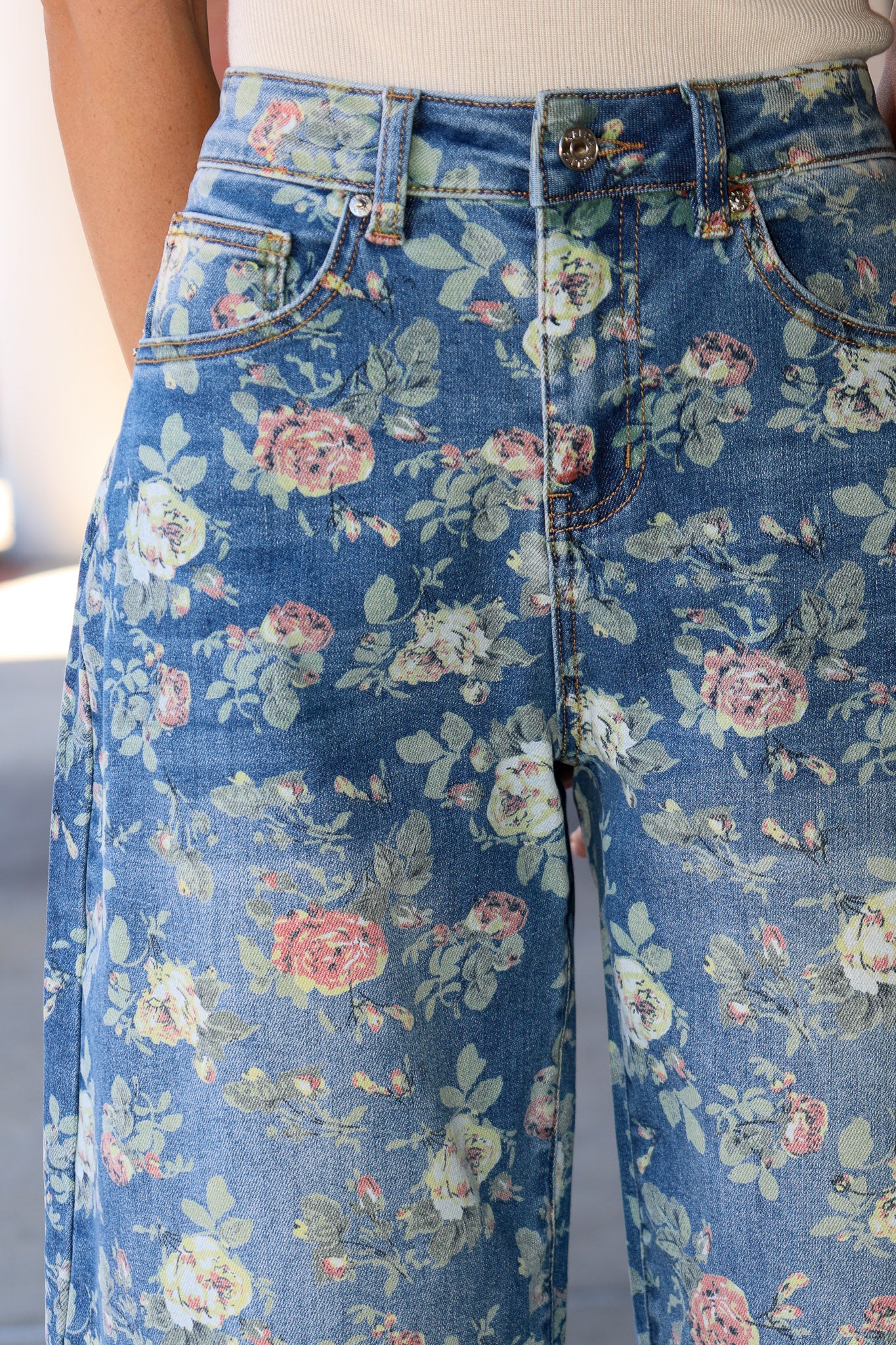 Close-up of a person wearing blue floral jeans with a pink and green rose print, paired with a light beige top.