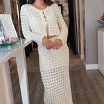 Woman wearing a white crochet outfit standing in a room with wooden flooring.