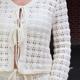 Close-up of a white crochet cardigan with a blurred background