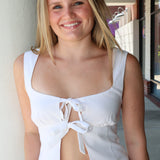Woman wearing a white sleeveless top with a bow detail, standing outdoors.