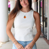 Woman wearing Celestine Tank a white sleeveless shirt with embroidered orange and denim shorts outdoors.
