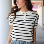 Woman wearing a black and white striped shirt with a collar, standing outdoors.