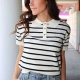 Woman wearing a black and white striped shirt with a collar, standing outdoors.