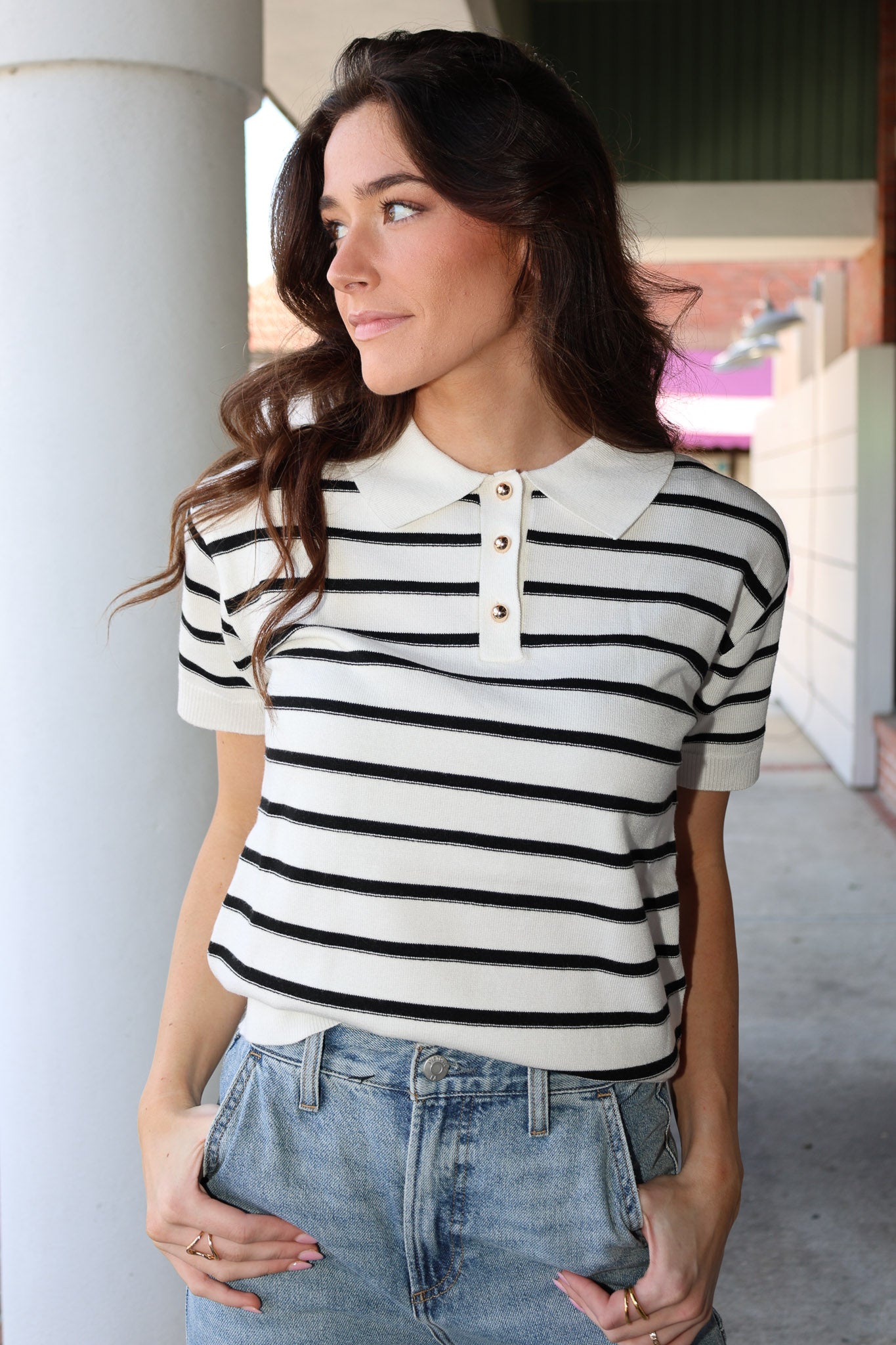 Woman wearing a black and white striped shirt with a collar, standing outdoors.