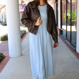 A woman wearing a light blue Charlotte midi dress by ZSupply with a dark brown leather jacket, and brown leather boots for a fall look.