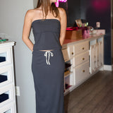 Woman wearing a strapless black two piece set  in a room with neon signs and furniture.