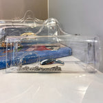 A clear plastic clutch bag with a silver metallic handle, resting on a white surface with a blue book in the background.