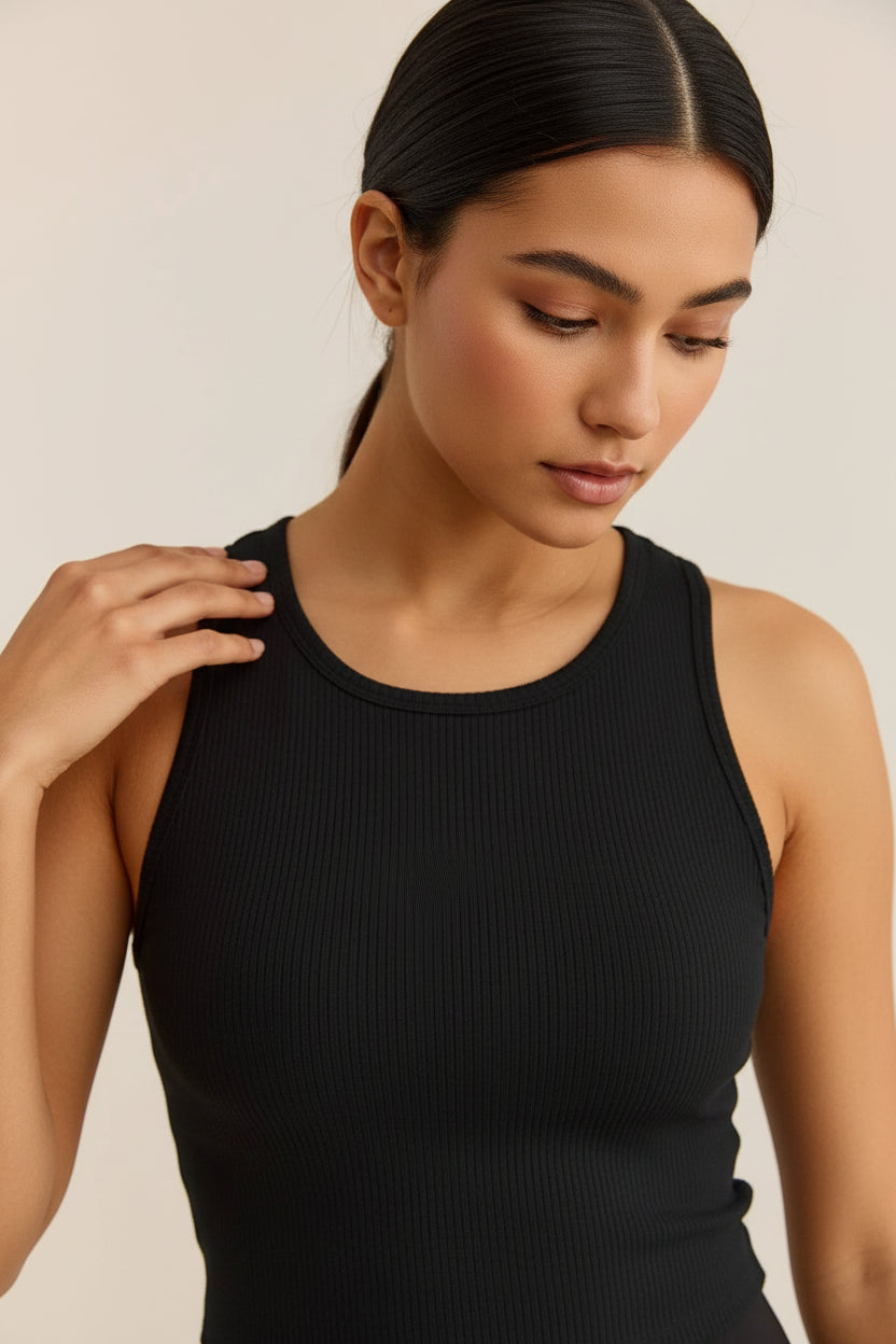 A woman wearing a black ribbed tank top, shown from the chest up against a plain light beige background.