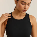 A woman wearing a black ribbed tank top, shown from the chest up against a plain light beige background.