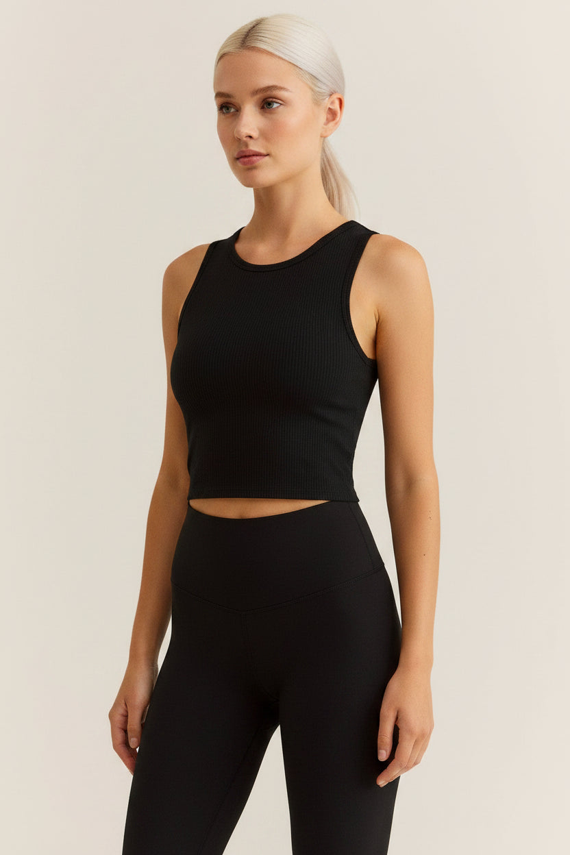 A woman modeling a black ribbed sleeveless tank top and matching black leggings against a plain light beige studio background.