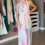 Woman wearing a colorful dress standing in a room with clothing racks and furniture.