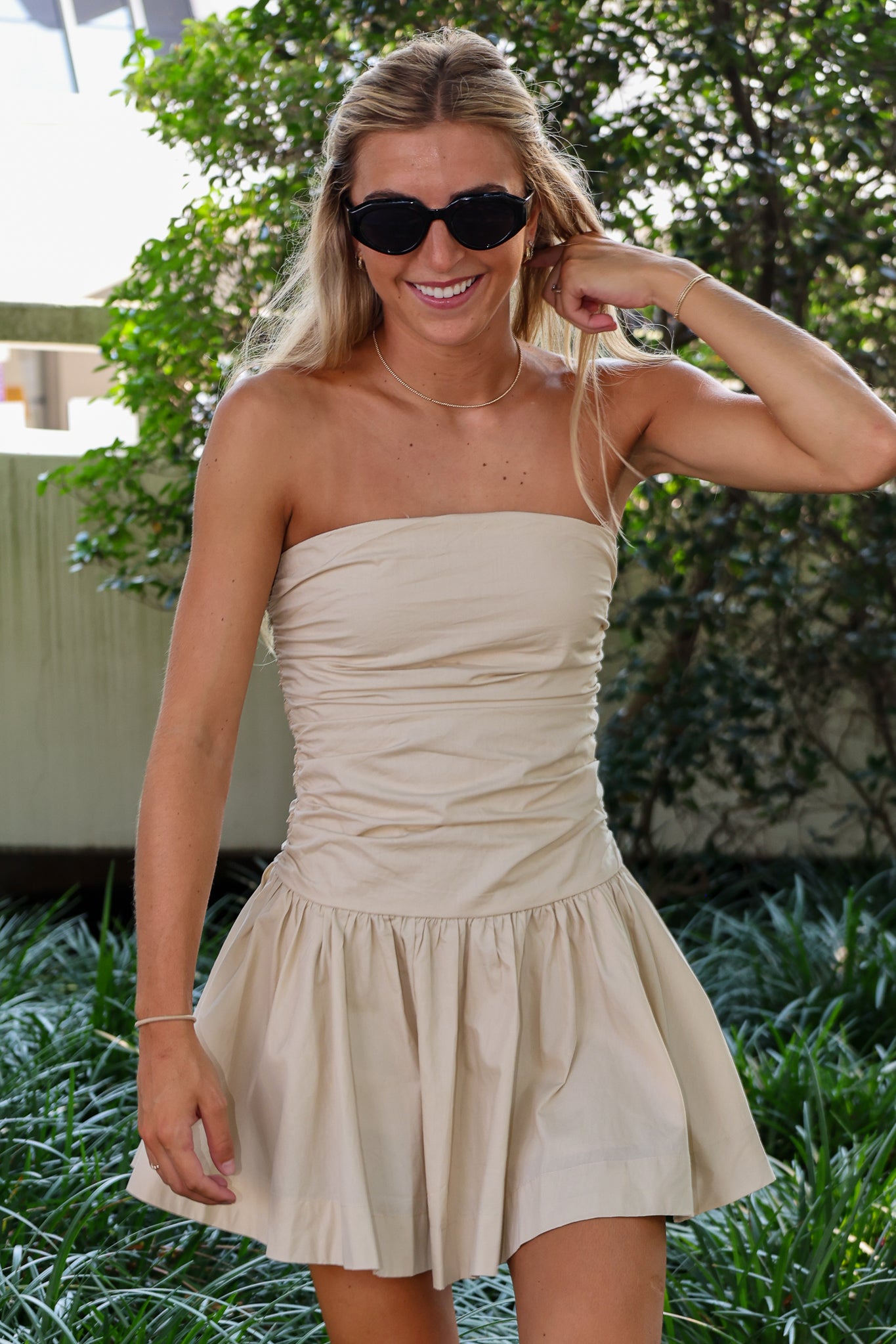 Woman wearing a beige strapless dress and sunglasses outdoors.
