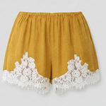 Mustard yellow shorts with white lace trim on a light gray background