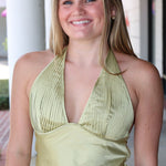 Woman wearing a green halter top and blue jeans standing outdoors.