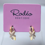 A pair of gold and silver gold butterfly hoop earrings with clear crystals, displayed on a pink 'Rodéo Boutique' card.