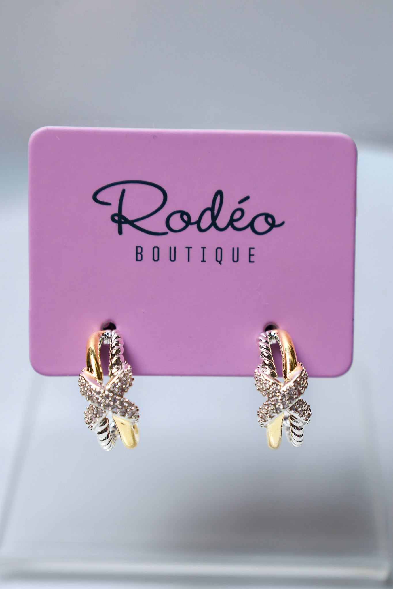 A pair of gold and silver gold butterfly hoop earrings with clear crystals, displayed on a pink 'Rodéo Boutique' card.