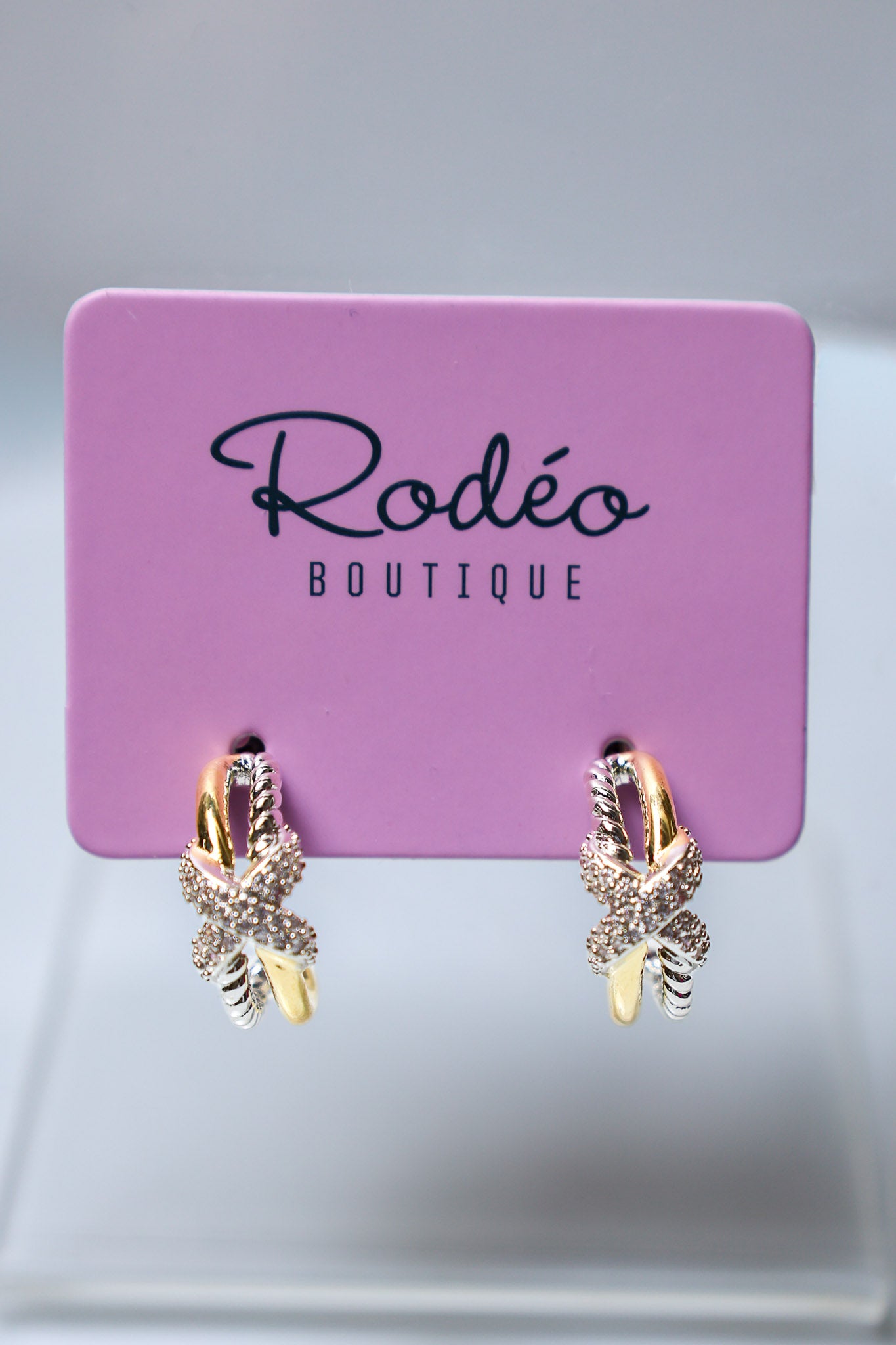 A pair of gold and silver gold butterfly hoop earrings with clear crystals, displayed on a pink 'Rodéo Boutique' card.
