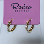 A pair of small gold hoop earrings covered with small clear rhinestones, hanging from a pink display card printed with the brand name 'Rodéo Boutique'.