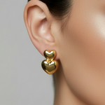 Close-up of a woman wearing gold heart-shaped earrings against a neutral background