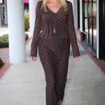 A smiling blonde woman wearing the Amara brown long-sleeve V-neck top with white polka dots by Z Supply and a tie-front detail, paired with a matching brown mesh midi Eda polka-dot skirt at Rodeo Boutique.