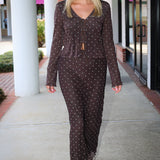 A smiling blonde woman wearing the Amara brown long-sleeve V-neck top with white polka dots by Z Supply and a tie-front detail, paired with a matching brown mesh midi Eda polka-dot skirt at Rodeo Boutique.